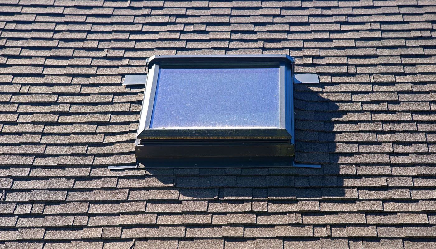 Blue skylight window on a shingled roof casting a shadow