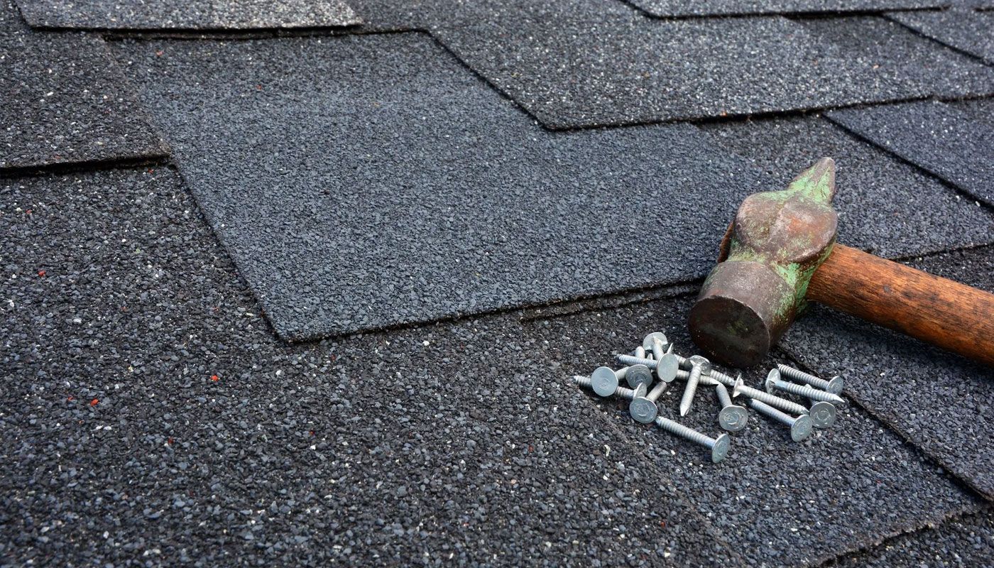 Roof shingles with a hammer and scattered roofing nails on top