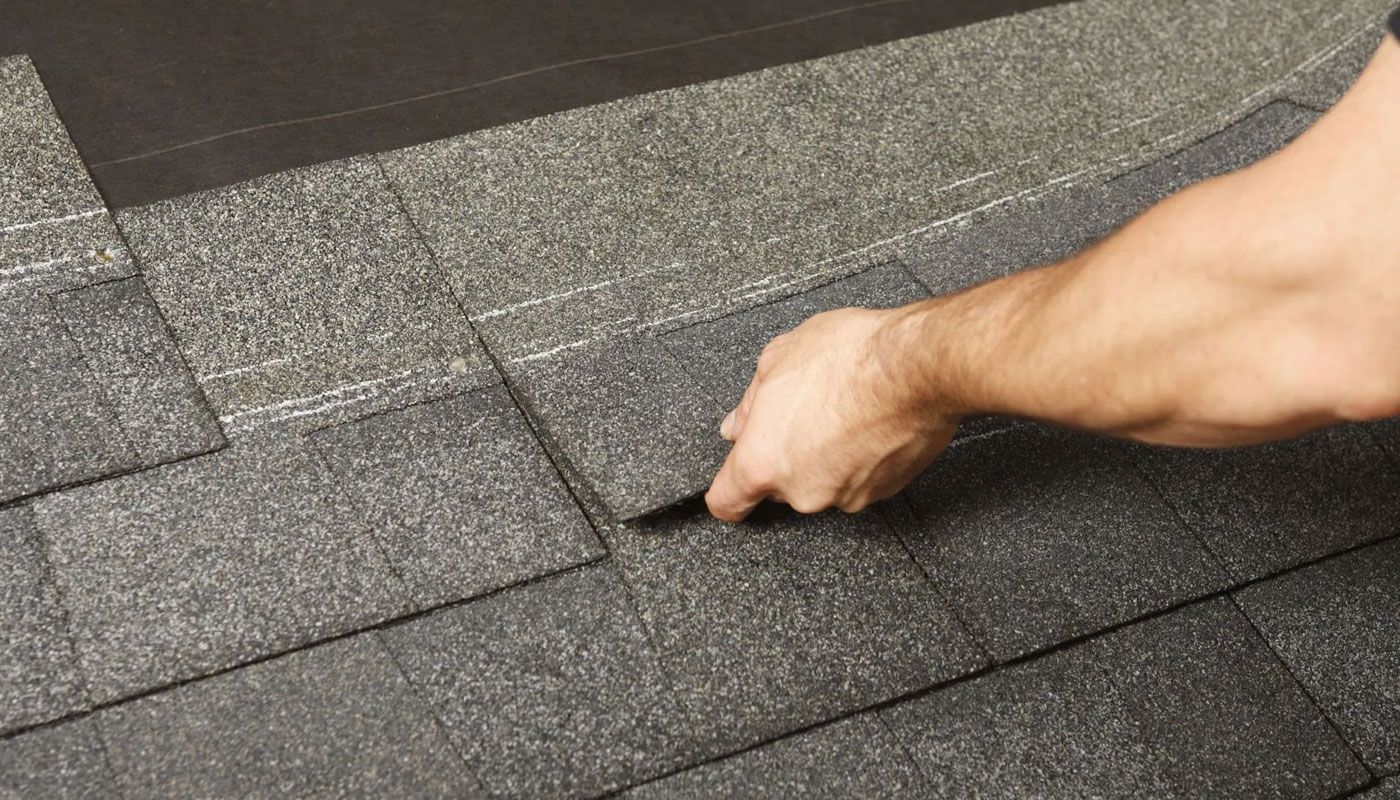 Hand checking dark gray roof shingles for damage or alignment