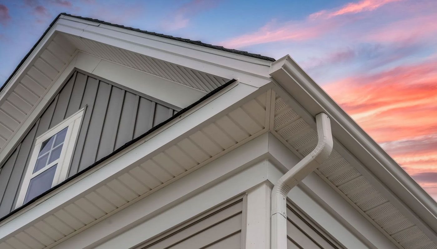 Gray house siding and white trim with a sloped roof against a pink sunset sky