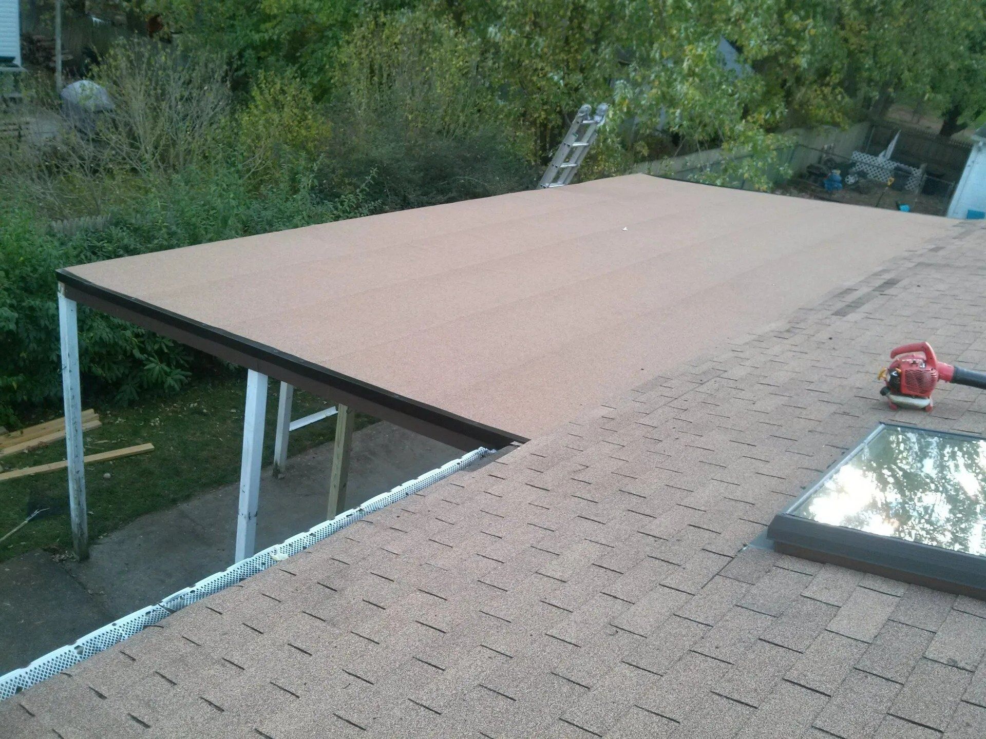 Rooftop with tan flat roof section beside a shingled roof, tools visible near the edge.