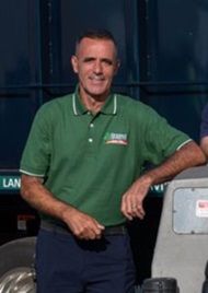 Man in green shirt, smiling, leaning on a recycling truck.
