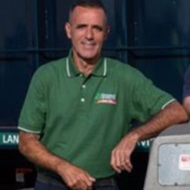 Man in green shirt, smiling, leaning on a recycling truck.