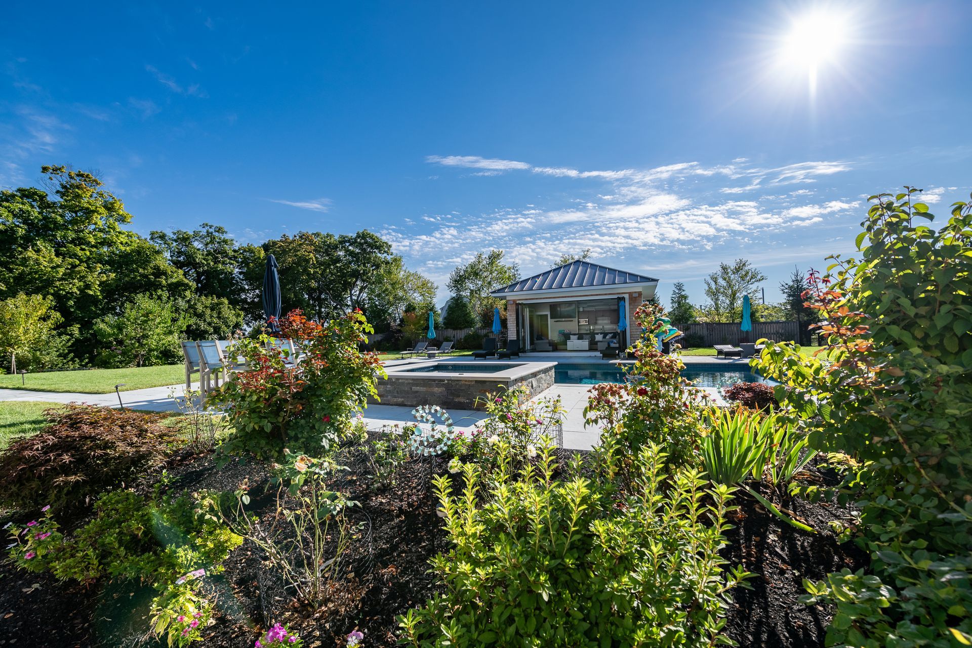 Landscaped backyard with pool, gazebo, and sunny sky.