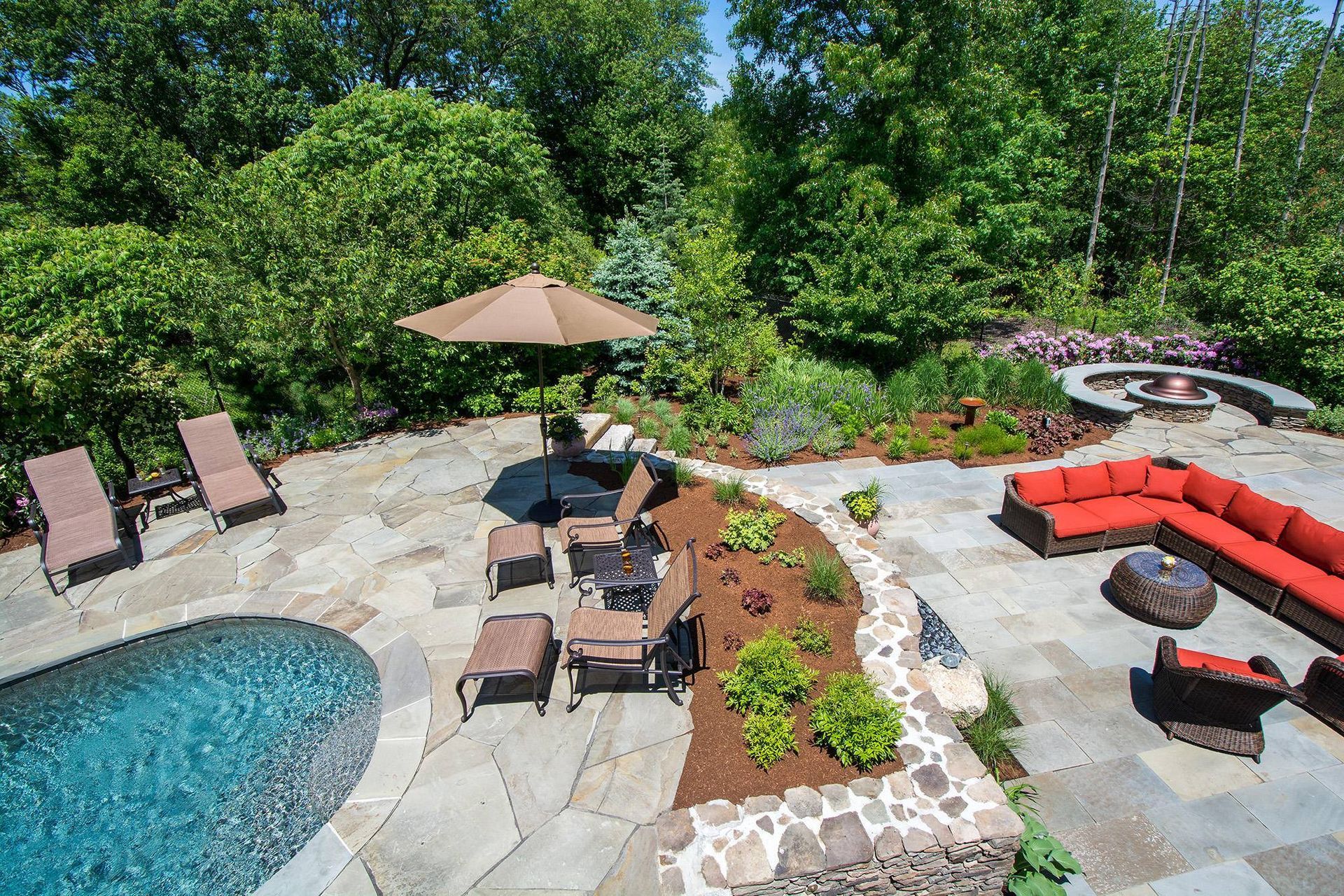 Backyard patio with pool, lounge chairs, seating area, and fire pit surrounded by trees.