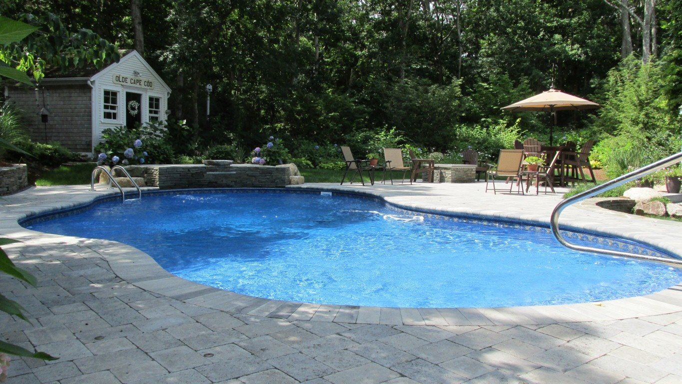 Swimming pool with blue water, stone patio, small shed, and trees.