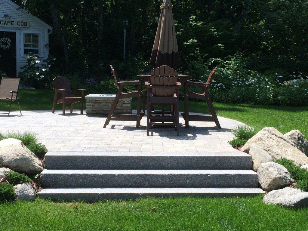 Stone steps lead to a patio with a table and chairs, near a small shed and greenery.