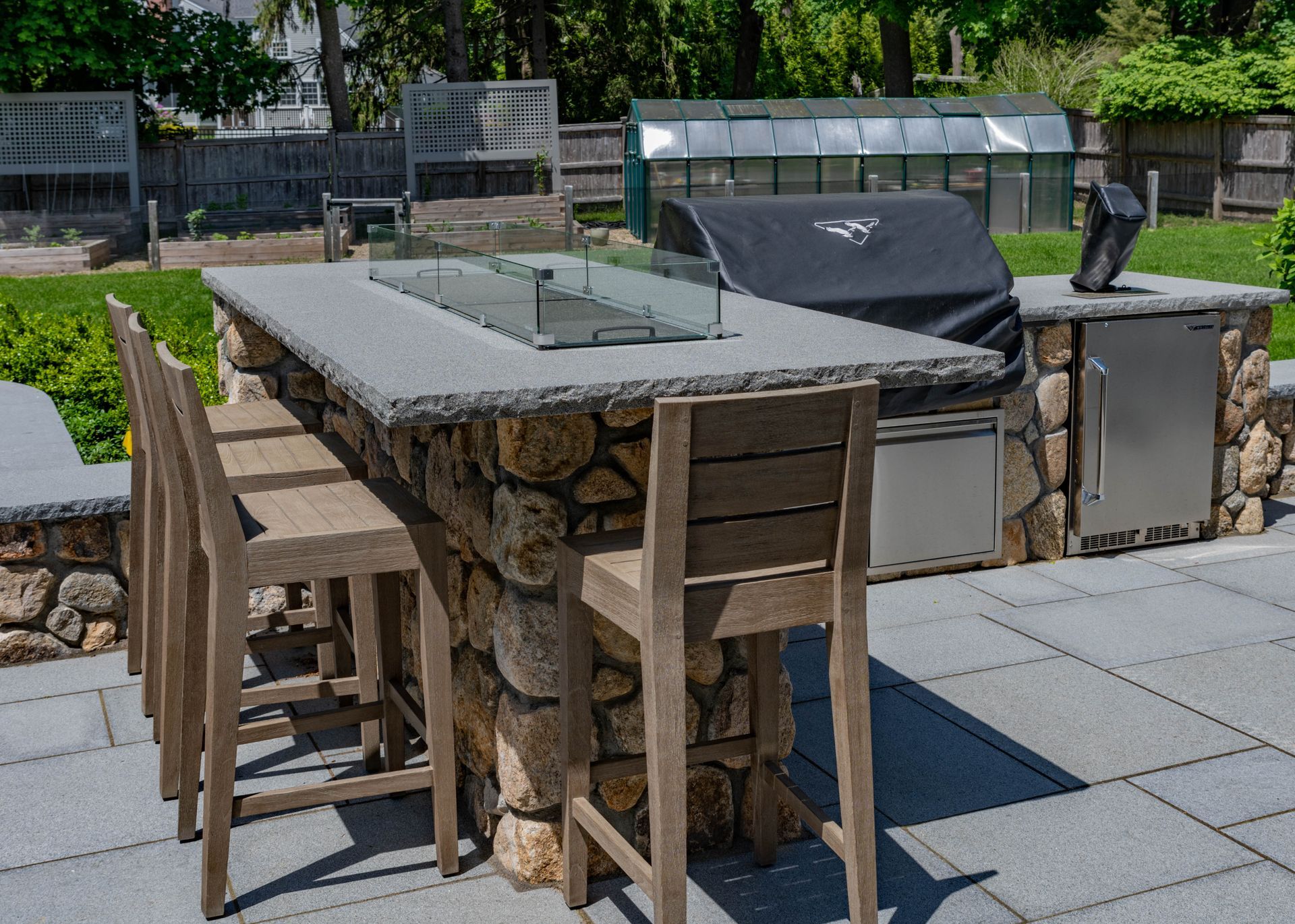 Outdoor kitchen with stone base, granite countertop, grill, fire pit, and bar stools.