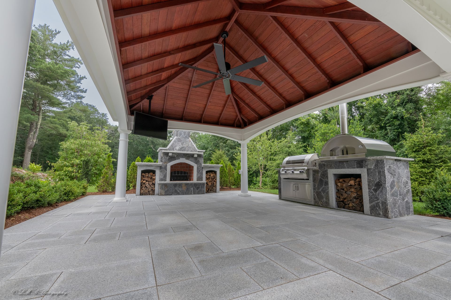 Outdoor patio with fireplace, grill, and wood-fired oven under a covered roof.