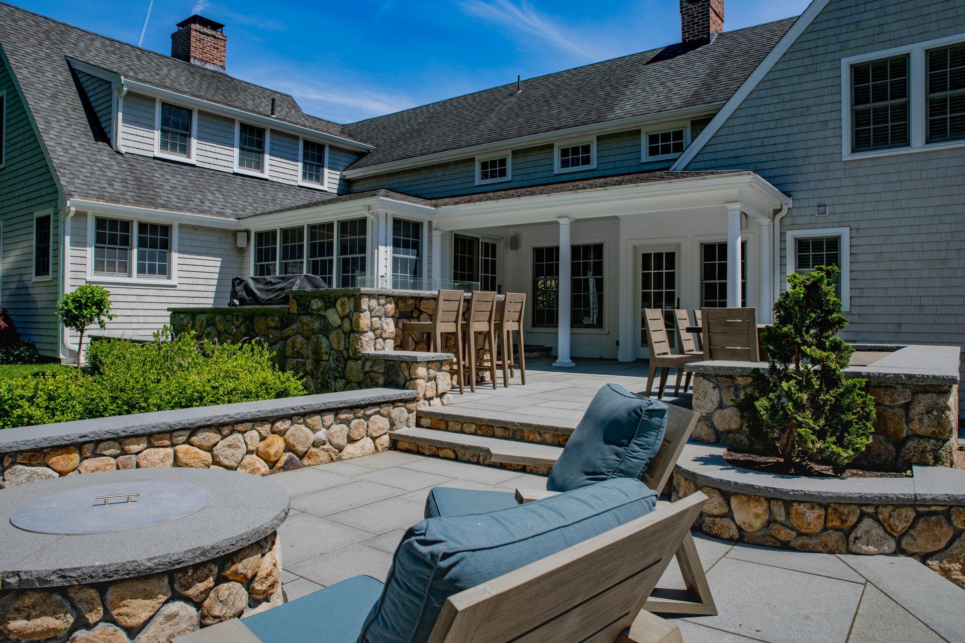 Outdoor patio with stone fire pit, seating, and access to a light blue house.