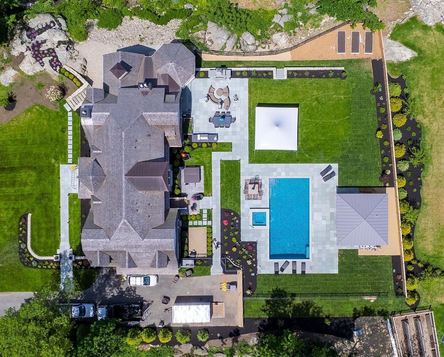 Aerial view of a large house with a pool, patio, and landscaped yard. Green grass, blue pool, gray roof.