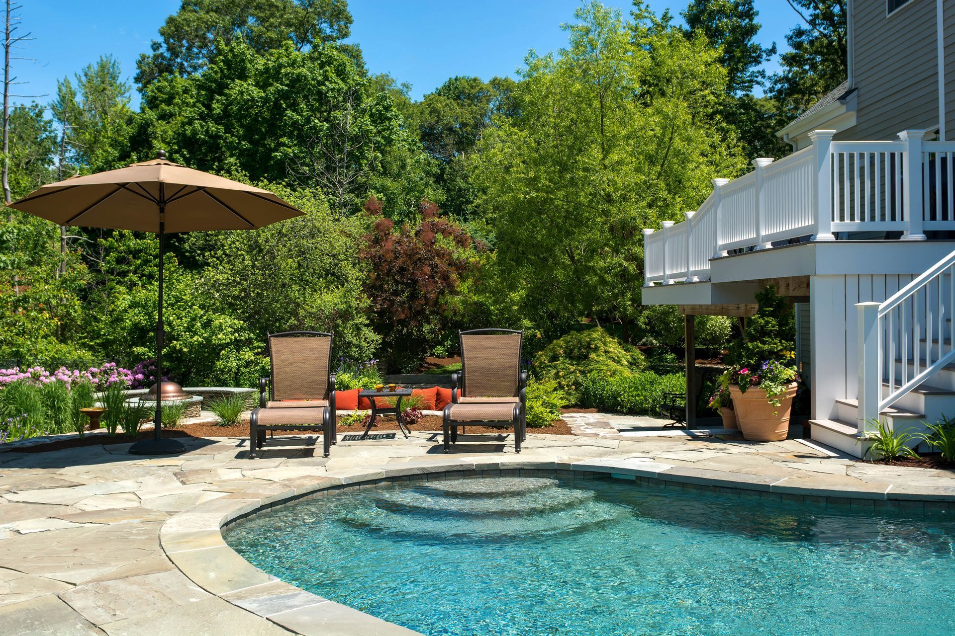 Poolside scene with pool, patio, chairs, umbrella, and lush greenery.