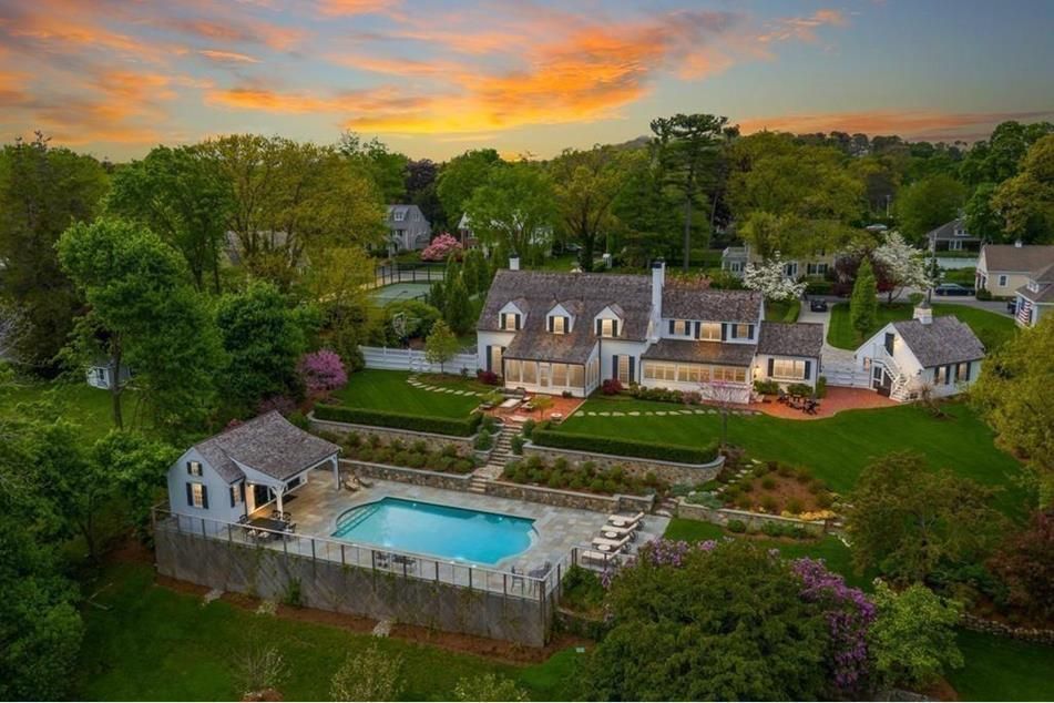 Aerial view of a large white house with a pool and a garden at sunset.