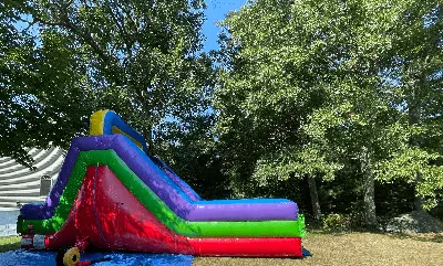 Colorful inflatable slide in a leafy backyard with red, green, purple, and yellow sections