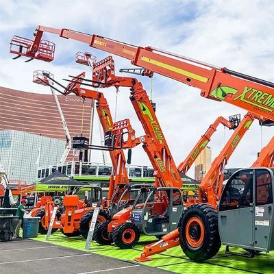 Bright orange cherry pickers and boom lifts on display at an outdoor trade show