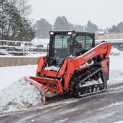 Orange Kubota skid steer clearing snow on a snowy street