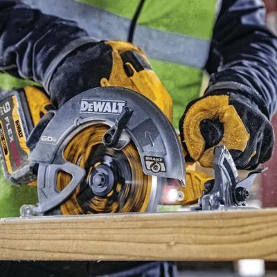Worker using a DEWALT circular saw to cut a wooden board, with dust and safety gloves visible