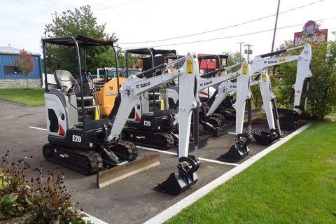 White mini excavators displayed outdoors on a paved lot, with grass and a dealership sign in the background