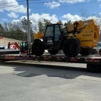 Yellow construction loader on a flatbed trailer outdoors under a blue sky.