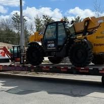 Yellow JCB telehandler secured on a flatbed trailer outdoors under a partly cloudy sky