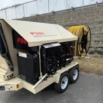Portable industrial machine trailer with tan cover, black components, and large hose reel on a roadside