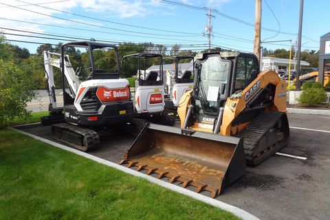 Compact excavators and a skid steer with a front bucket parked beside a grassy roadside