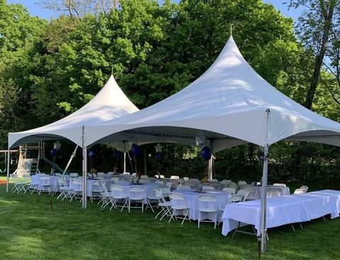 White event tents with tables and chairs set up on a grassy lawn beside trees