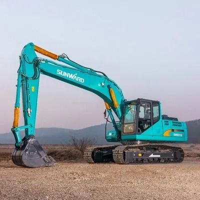 Turquoise excavator on a dirt field with mountains in the background