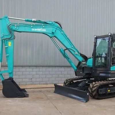 Turquoise Sunward excavator with front blade parked beside a gray industrial wall