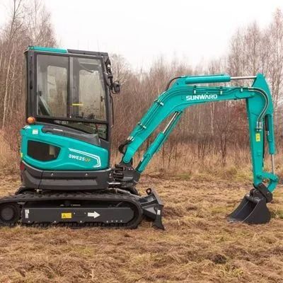 Turquoise mini excavator parked on muddy ground beside bare trees