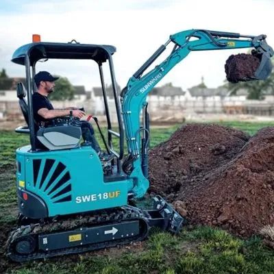 Blue mini excavator loading dirt into a pile on a grassy construction site
