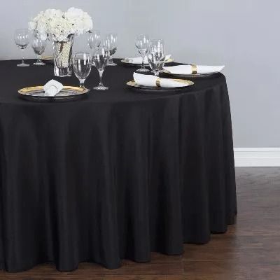 Round banquet table with black linen, white floral centerpiece, and place settings of glassware and plates