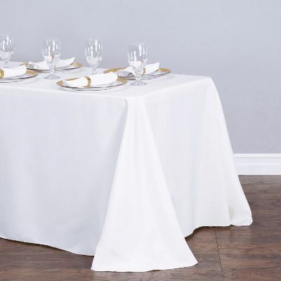 White tablecloth draped over a dining table set with plates and glassware against a light gray wall