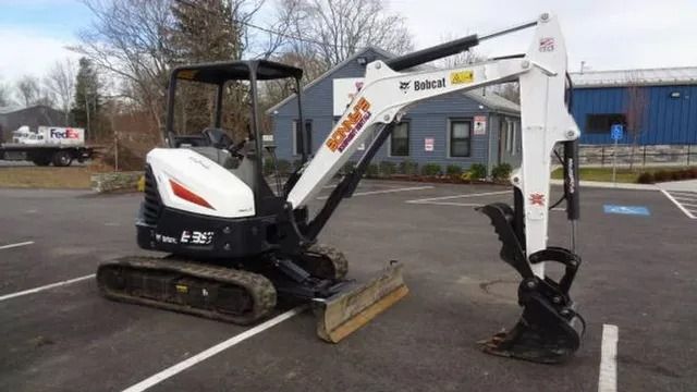 White mini excavator with a bucket attachment parked in a lot near a building