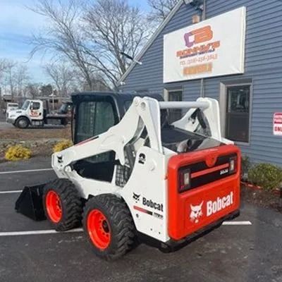 Bobcat skid-steer loader parked outside a blue building with a company sign.