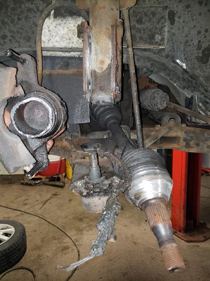 Damaged vehicle suspension components, including axle, steering knuckle, and control arm. Black and gray metal.