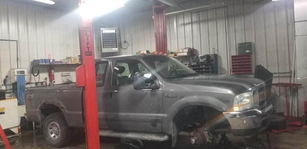 A gray pickup truck in a mechanic shop, raised on a lift. Red lift post in the foreground.