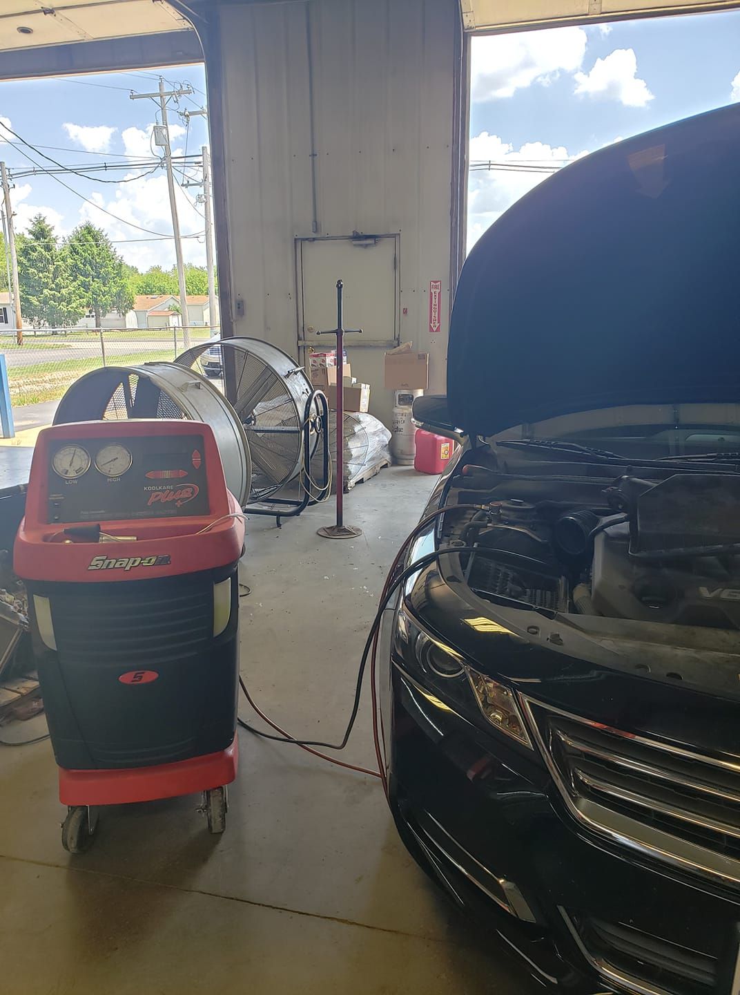 Car in auto shop with hood open, connected to a red and black AC service machine.