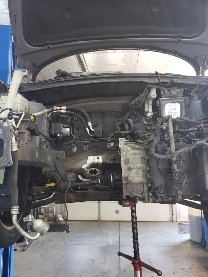 Car chassis raised on a lift, engine compartment exposed, tools and garage setting.