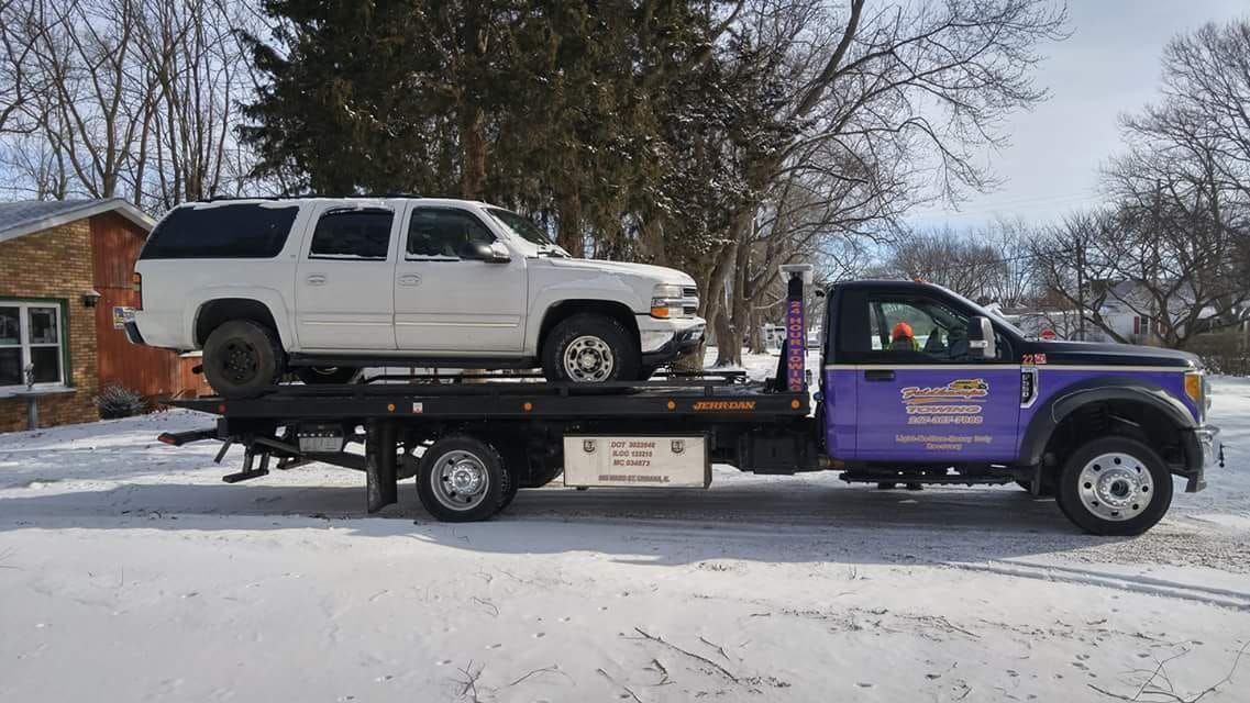 White SUV being towed on a flatbed truck in a snowy environment.