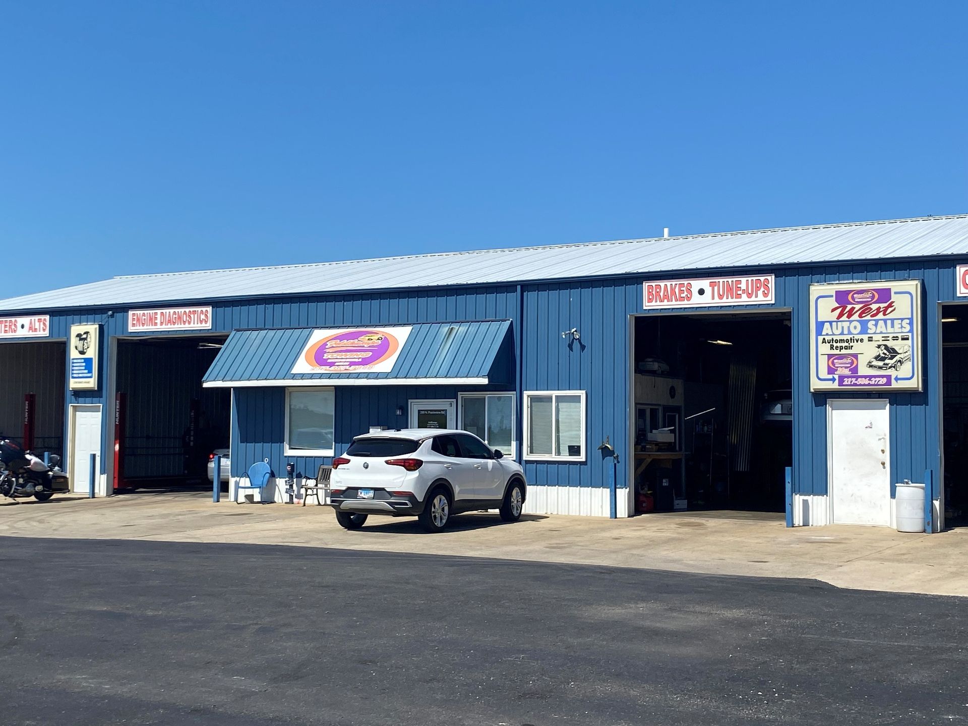 Blue auto repair shop with white car parked out front on a sunny day.