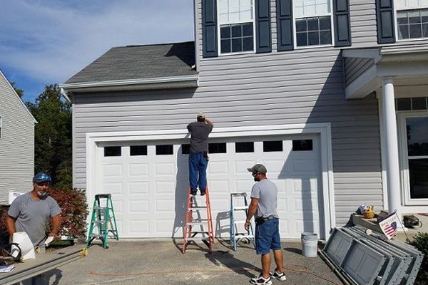 Two men are working on a garage door in front of a house.