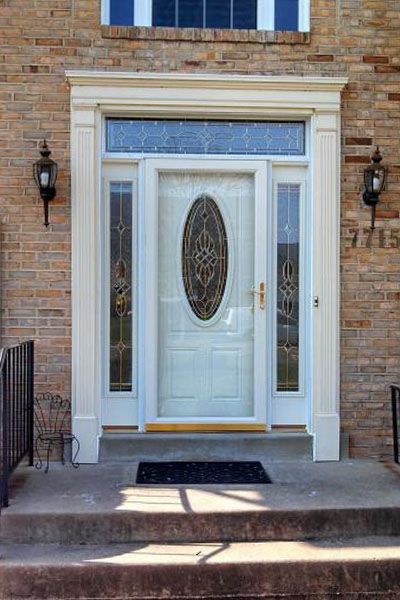 The front door of a brick house with a white door and stained glass windows.