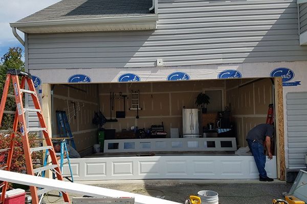 A man is working on a garage door in front of a house.
