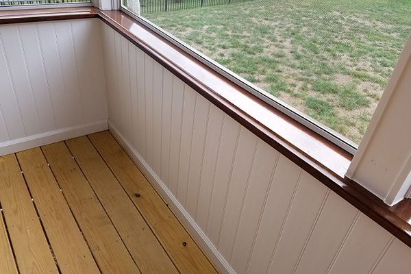 A screened in porch with a large window and a wooden floor.