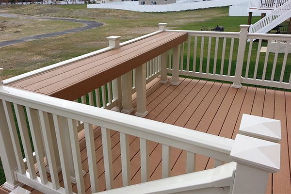 A wooden deck with a white railing and a bench