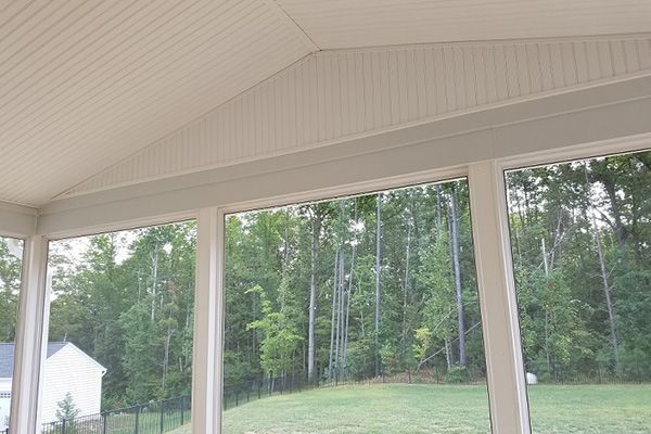 A screened in porch with a view of a lush green field and trees.