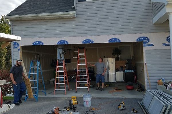 Two men are working on a garage door with a ladder