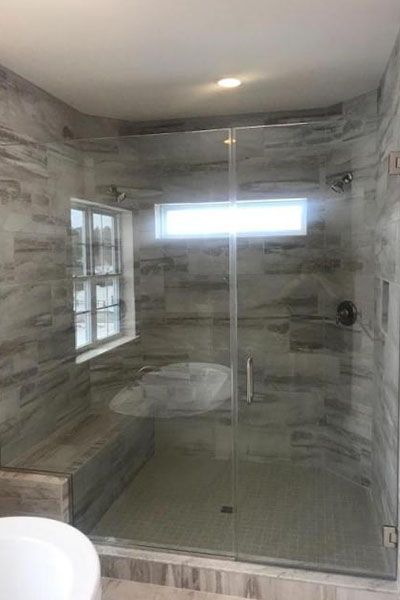 A bathroom with a walk in shower with a glass door and a window.