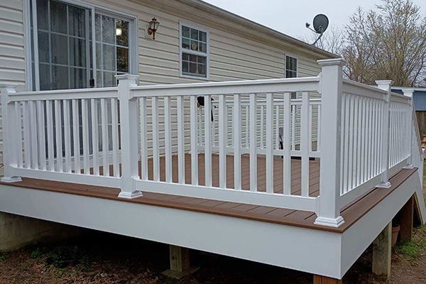 A deck with a white railing is in front of a mobile home.